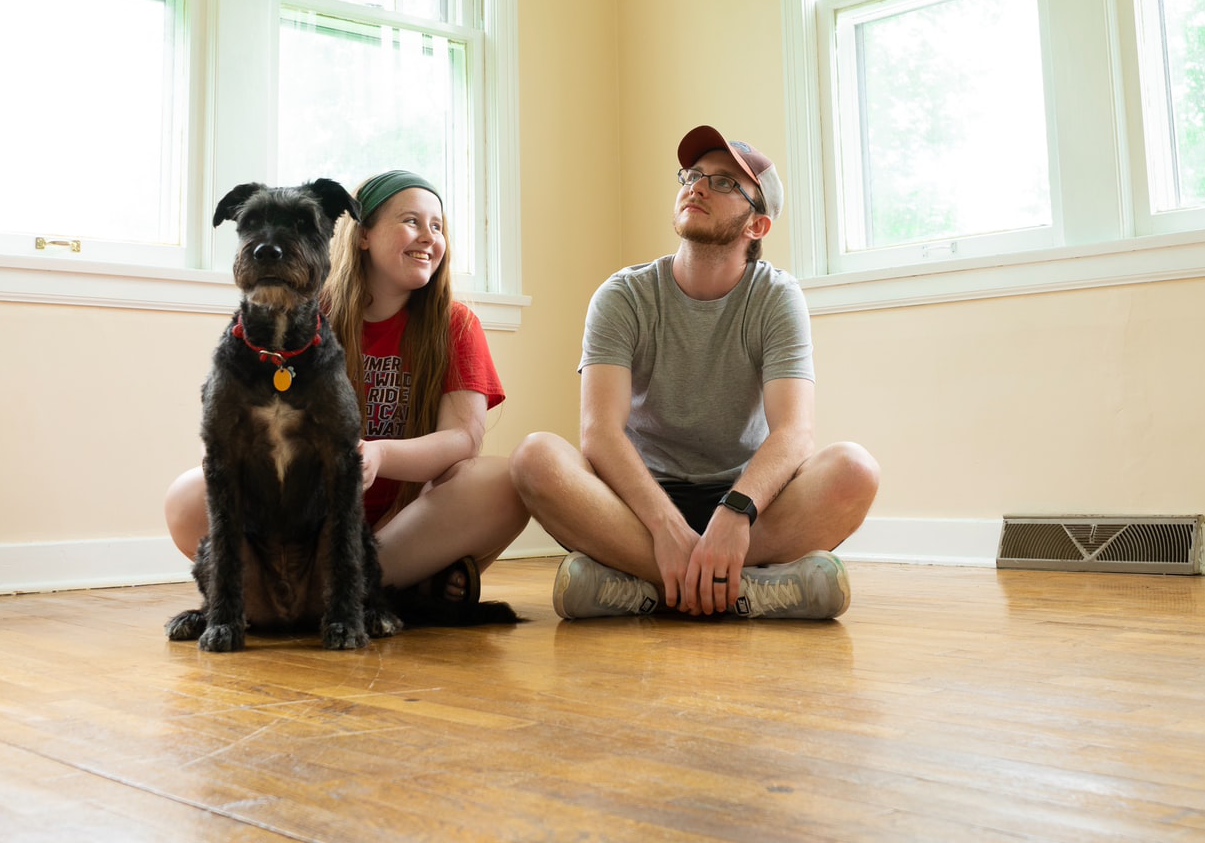 Stock image of young couple sitting and smiling in an empty house with their dog.