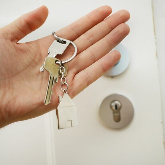 Stock image of a hand holding a set of keys with a house-shaped keychain.